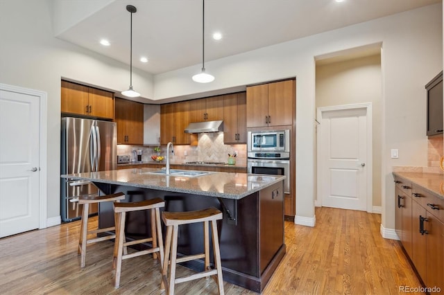 kitchen featuring appliances with stainless steel finishes, under cabinet range hood, a sink, stone counters, and tasteful backsplash