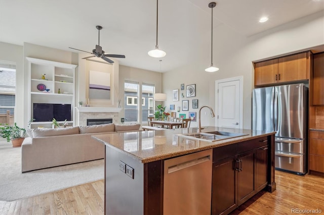 kitchen featuring stainless steel appliances, a sink, light wood-style flooring, ceiling fan, and decorative light fixtures