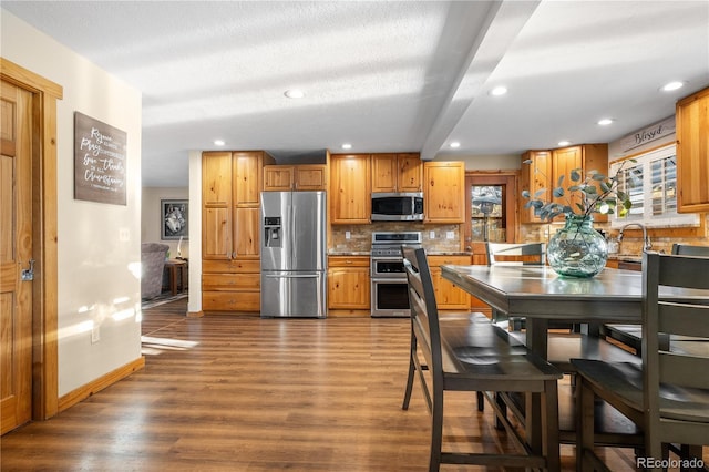 kitchen featuring dark wood-type flooring, stainless steel appliances, decorative backsplash, and a textured ceiling