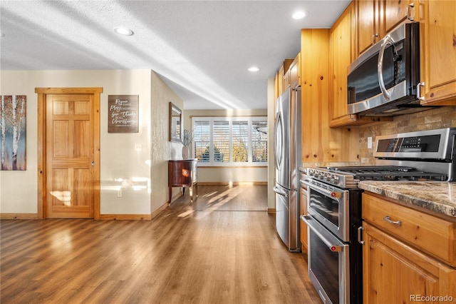 kitchen featuring stainless steel appliances, tasteful backsplash, hardwood / wood-style floors, and dark stone countertops