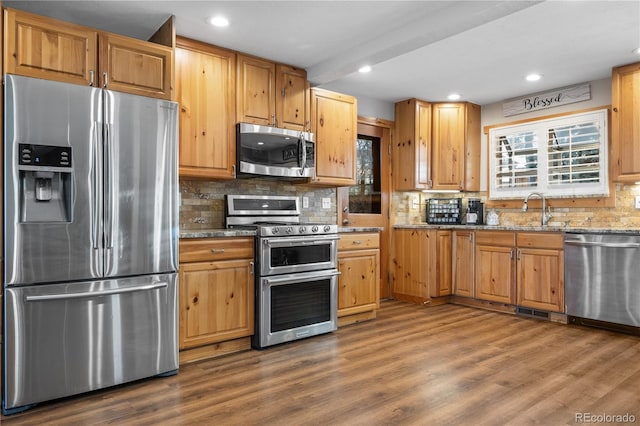 kitchen featuring sink, dark wood-type flooring, stainless steel appliances, light stone countertops, and decorative backsplash