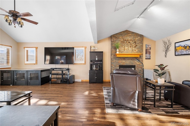 living room featuring vaulted ceiling, a stone fireplace, dark hardwood / wood-style floors, rail lighting, and ceiling fan