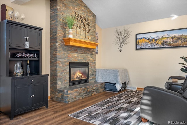 living room featuring lofted ceiling, a stone fireplace, and dark wood-type flooring