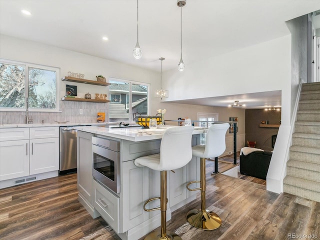 kitchen featuring dishwasher, white cabinets, hanging light fixtures, light stone countertops, and dark hardwood / wood-style flooring