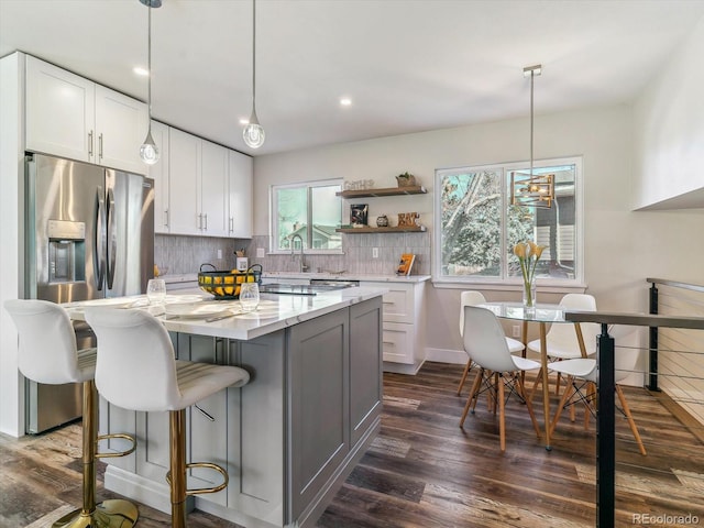 kitchen with white cabinetry, hanging light fixtures, a kitchen island, and light stone countertops