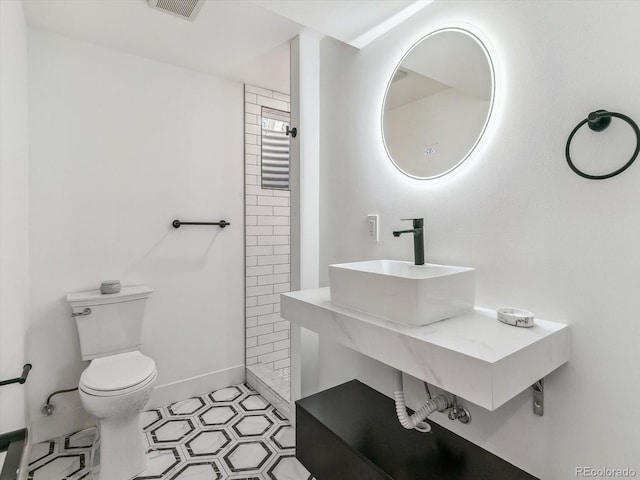 bathroom featuring a tile shower, toilet, and sink