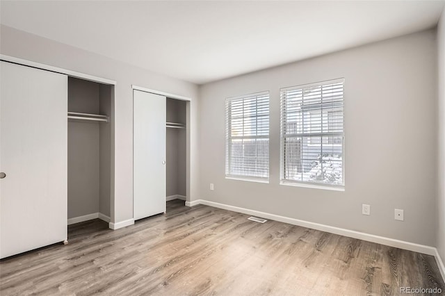 unfurnished bedroom featuring multiple closets and light wood-type flooring