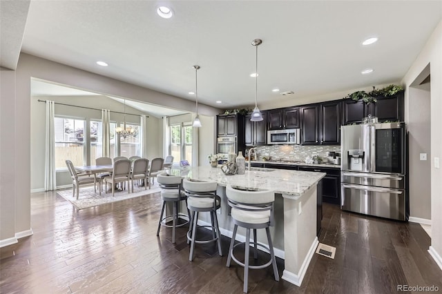 12631 Glencoe St, Thornton, CO 80241 - kitchen with appliances with stainless steel finishes, an island with sink, decorative backsplash, light stone counters, and dark wood-style floors