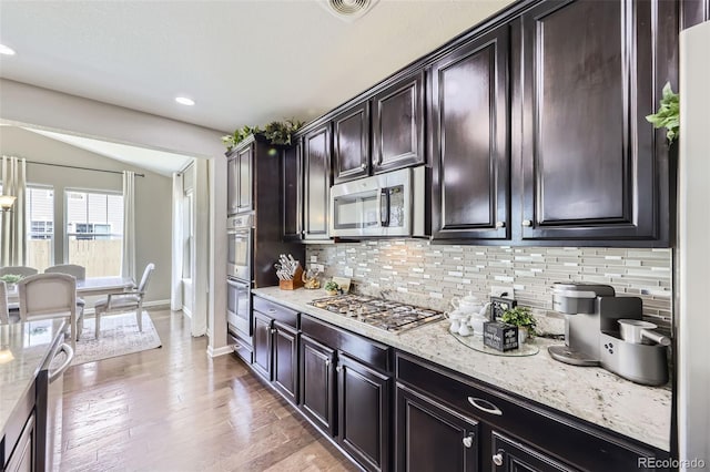 12631 Glencoe St, Thornton, CO 80241 - kitchen featuring stainless steel appliances, decorative backsplash, vaulted ceiling, light stone countertops, and light wood finished floors