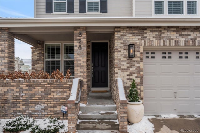 snow covered property entrance with brick siding and an attached garage