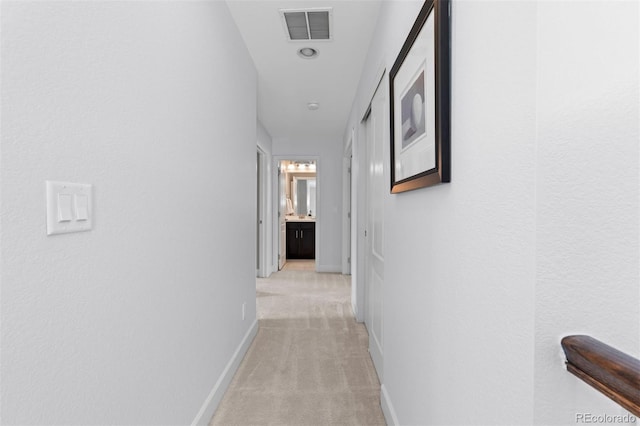 hall featuring light carpet, baseboards, and visible vents