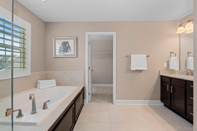 full bath with a garden tub, a spacious closet, vanity, tile patterned flooring, and baseboards