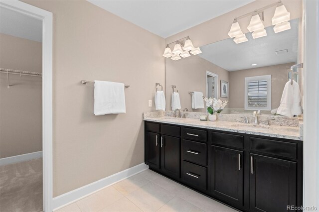 full bath with double vanity, a spacious closet, baseboards, and a sink