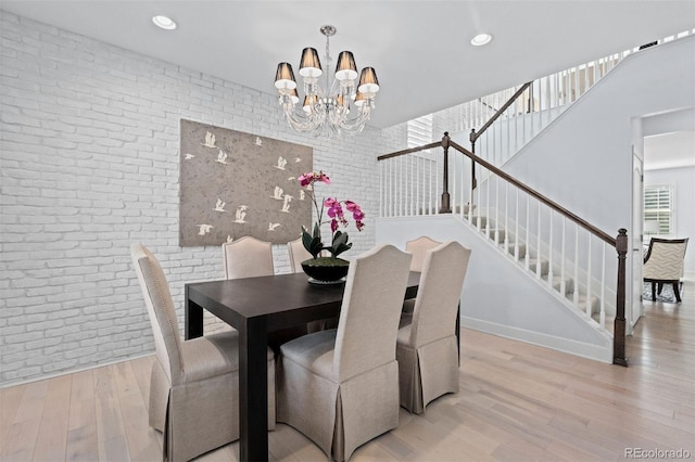 dining area featuring an inviting chandelier, brick wall, stairs, and light wood-style flooring