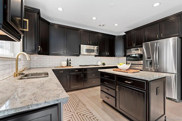 kitchen featuring appliances with stainless steel finishes, a sink, backsplash, and light stone counters