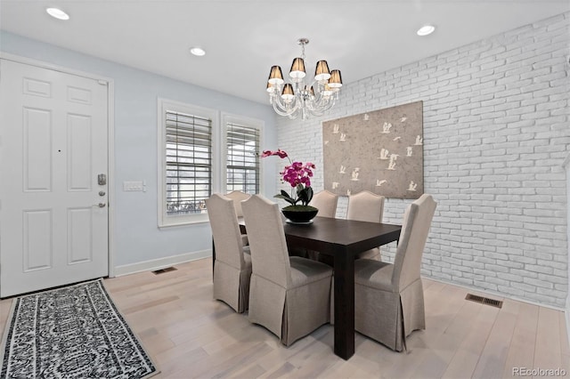 dining area featuring light wood finished floors, brick wall, visible vents, and a notable chandelier