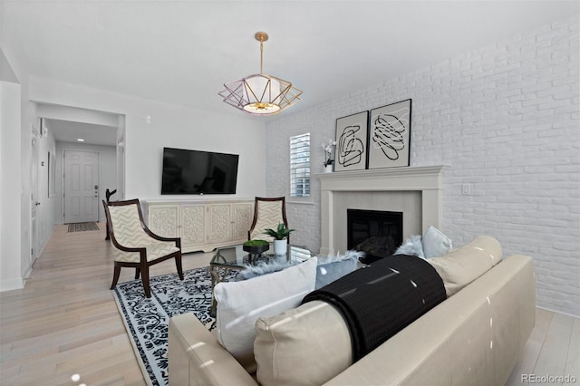 living area featuring baseboards, brick wall, a fireplace, and light wood-style floors