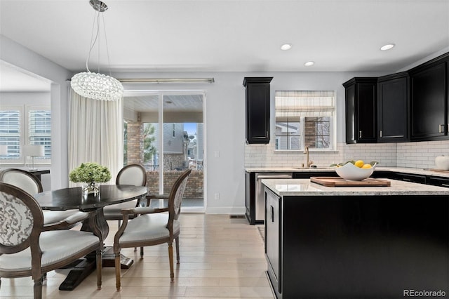 kitchen with a wealth of natural light, decorative backsplash, dark cabinetry, and decorative light fixtures