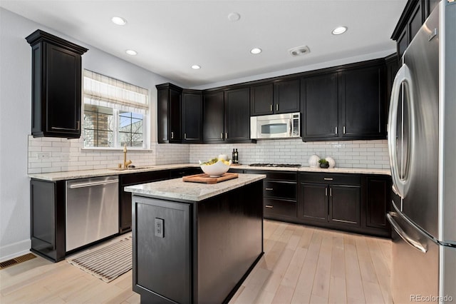 kitchen featuring light stone counters, a center island, light wood finished floors, stainless steel appliances, and a sink