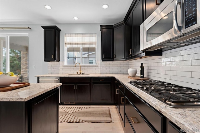 kitchen with appliances with stainless steel finishes, a healthy amount of sunlight, a sink, and light stone counters