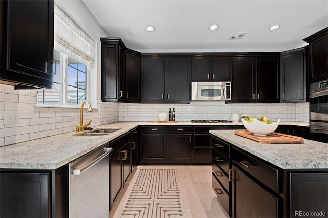 kitchen featuring tasteful backsplash, appliances with stainless steel finishes, a sink, and dark cabinets