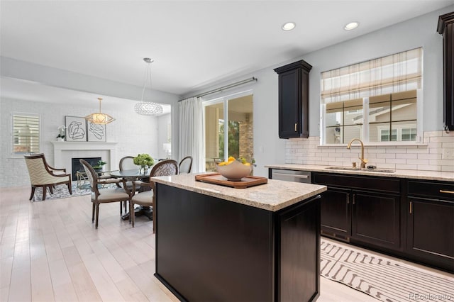 kitchen with light stone counters, a sink, a kitchen island, a glass covered fireplace, and decorative light fixtures