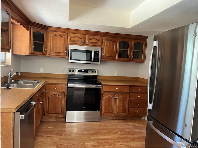 12252 Elmendorf Pl, Denver, CO 80239 - kitchen featuring appliances with stainless steel finishes, brown cabinetry, light wood-style floors, and glass insert cabinets