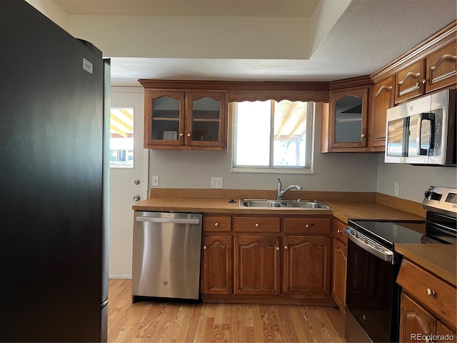 12252 Elmendorf Pl, Denver, CO 80239 - kitchen with appliances with stainless steel finishes, light wood finished floors, glass insert cabinets, and brown cabinets