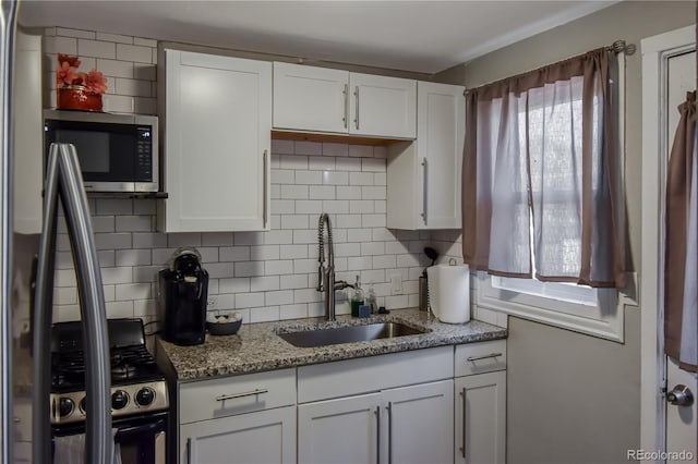 kitchen featuring sink, stainless steel appliances, white cabinets, light stone countertops, and decorative backsplash