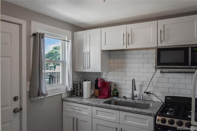 kitchen with sink, light stone counters, white cabinetry, gas range, and tasteful backsplash