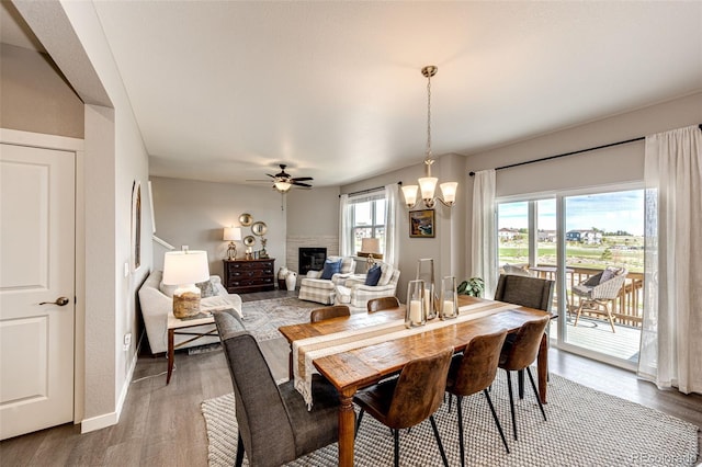 dining space featuring a fireplace, wood finished floors, a ceiling fan, and a chandelier
