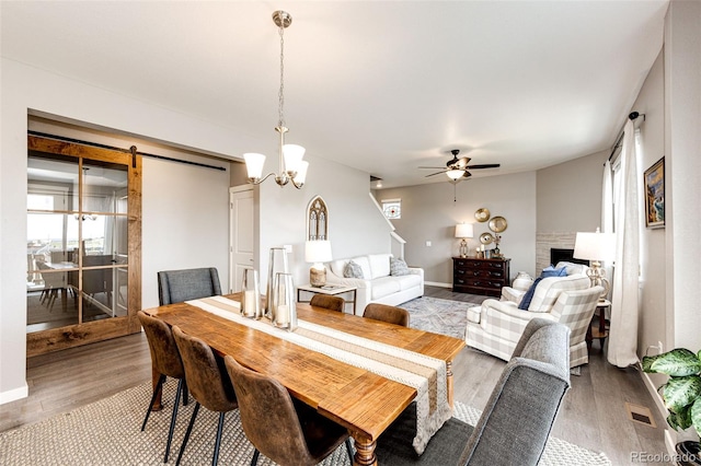dining space with light wood-style floors, ceiling fan, a chandelier, a barn door, and baseboards