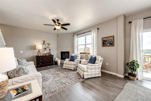 living room featuring wood finished floors, ceiling fan, a tile fireplace, and baseboards