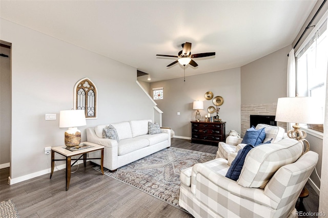 living area featuring a ceiling fan, wood finished floors, baseboards, and a fireplace