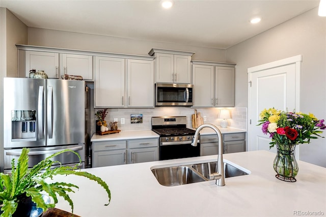 kitchen with stainless steel appliances, a sink, gray cabinetry, light countertops, and tasteful backsplash