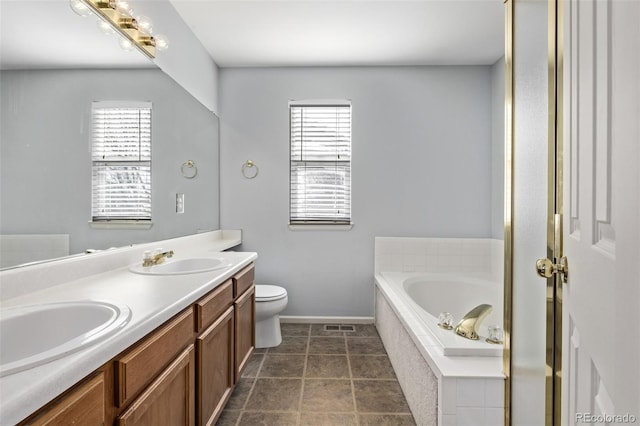 bathroom with toilet, a healthy amount of sunlight, tiled bath, and vanity