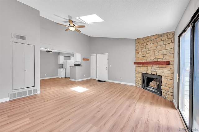 unfurnished living room with a ceiling fan, light wood-style floors, a fireplace, a textured ceiling, and a skylight