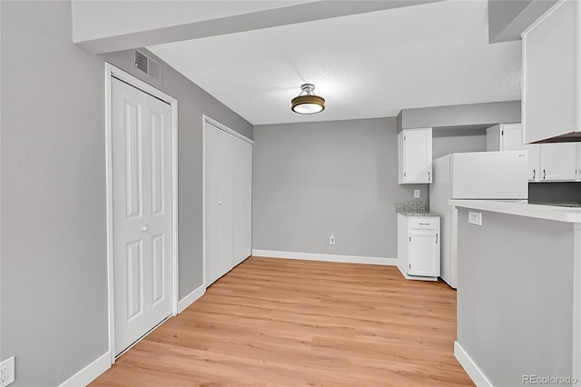 kitchen with freestanding refrigerator, white cabinets, light wood-style floors, baseboards, and a textured ceiling