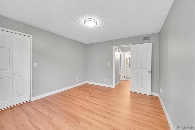 unfurnished bedroom with light wood-style floors, a textured ceiling, baseboards, and a closet