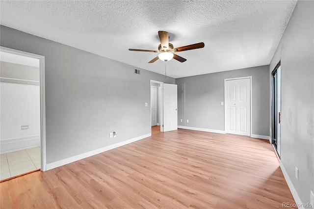 unfurnished bedroom with light wood finished floors, a textured ceiling, baseboards, ensuite bath, and a ceiling fan