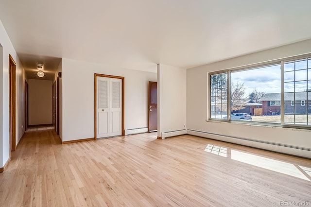 unfurnished room featuring a baseboard heating unit, baseboards, and light wood-style floors