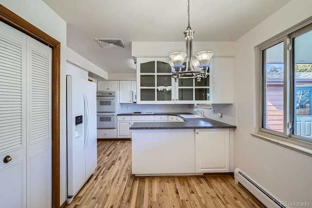 kitchen featuring dark countertops, visible vents, a baseboard heating unit, white appliances, and a sink