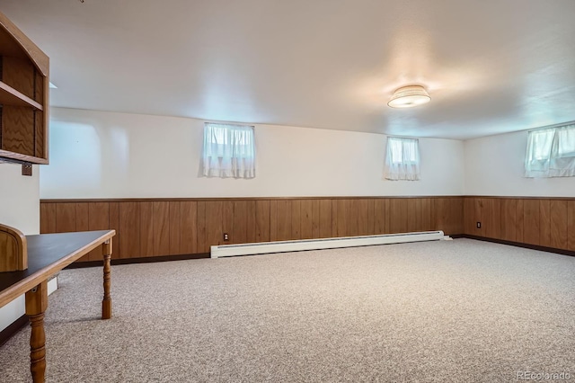 basement featuring a baseboard radiator, plenty of natural light, wooden walls, and wainscoting