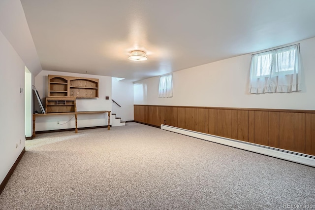 below grade area with a wealth of natural light, a wainscoted wall, light colored carpet, and a baseboard heating unit