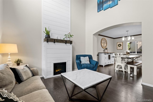 2066 Amber Ct, Erie, CO 80516 - living area featuring a chandelier, arched walkways, dark wood-type flooring, a large fireplace, and ornamental molding