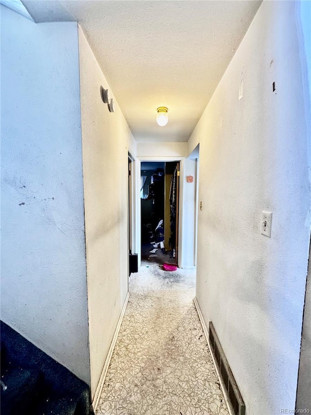 corridor with a textured wall, visible vents, and a textured ceiling