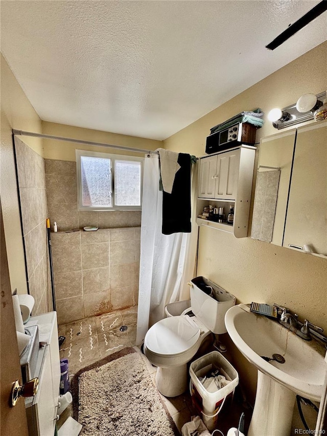 bathroom with a sink, toilet, a stall shower, and a textured ceiling