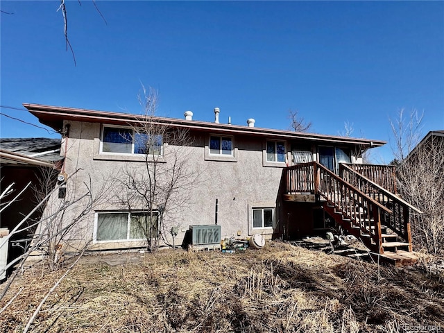 rear view of house with stucco siding, central air condition unit, and stairs