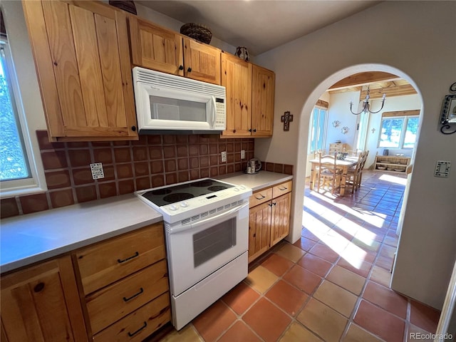 kitchen featuring arched walkways, light tile patterned flooring, white appliances, light countertops, and backsplash