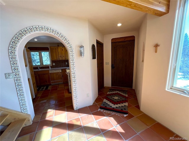 corridor featuring arched walkways, plenty of natural light, dark tile patterned floors, and recessed lighting